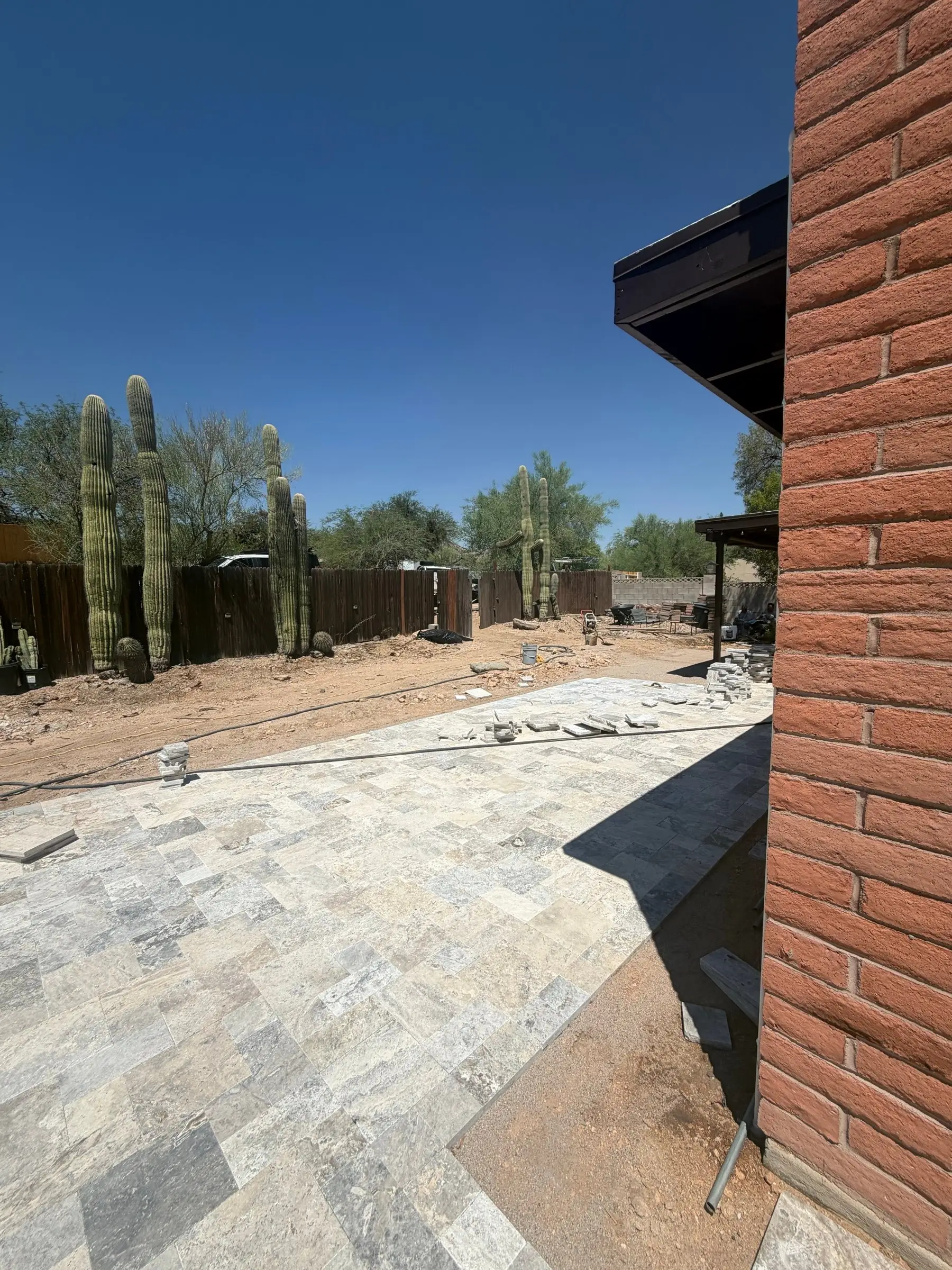 Silver travertine pool deck being laid beside a brick home with tall saguaros