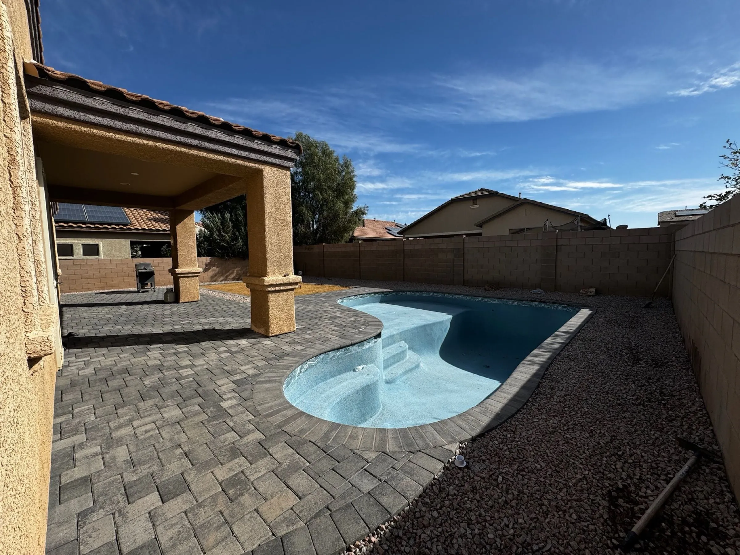 Small freeform pool with entry steps, gray paver deck and covered patio in a Marana backyard.
