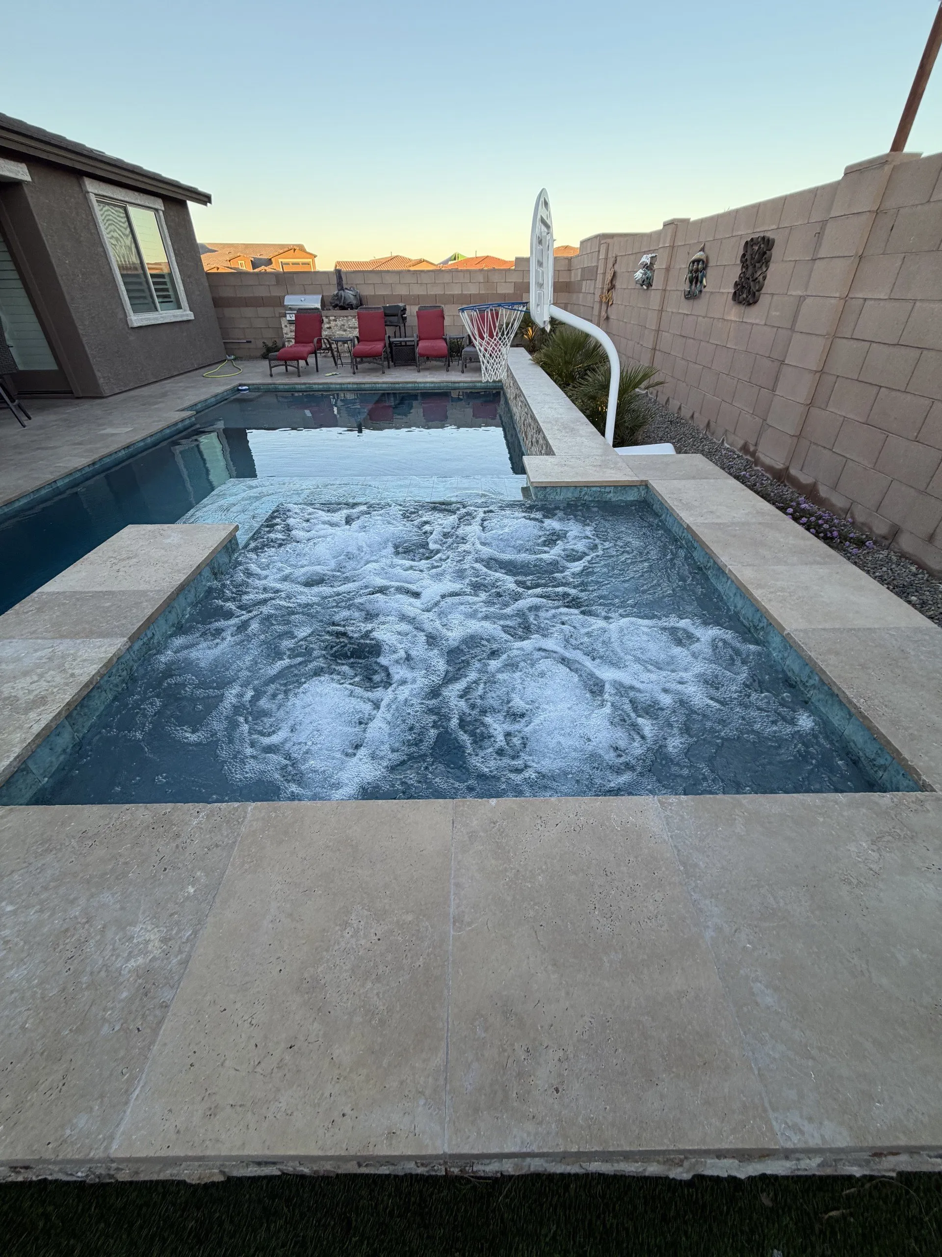 Spa jets running in a raised spa with travertine coping and the pool beyond at dusk.