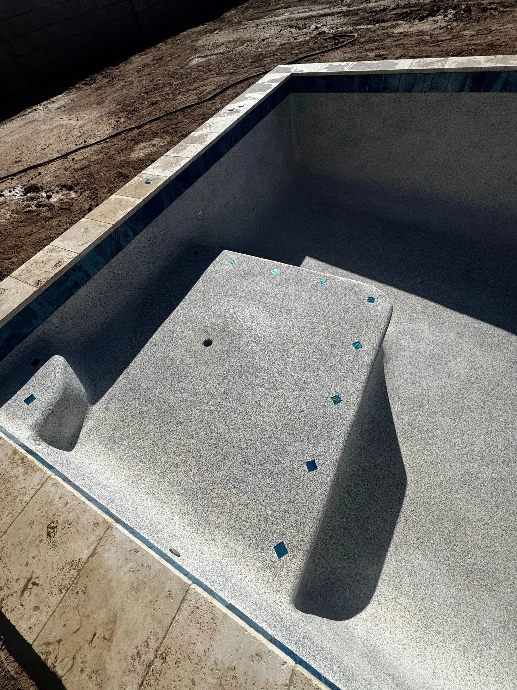 Close view of a new speckled finish on pool entry steps and a bench with blue step markers.