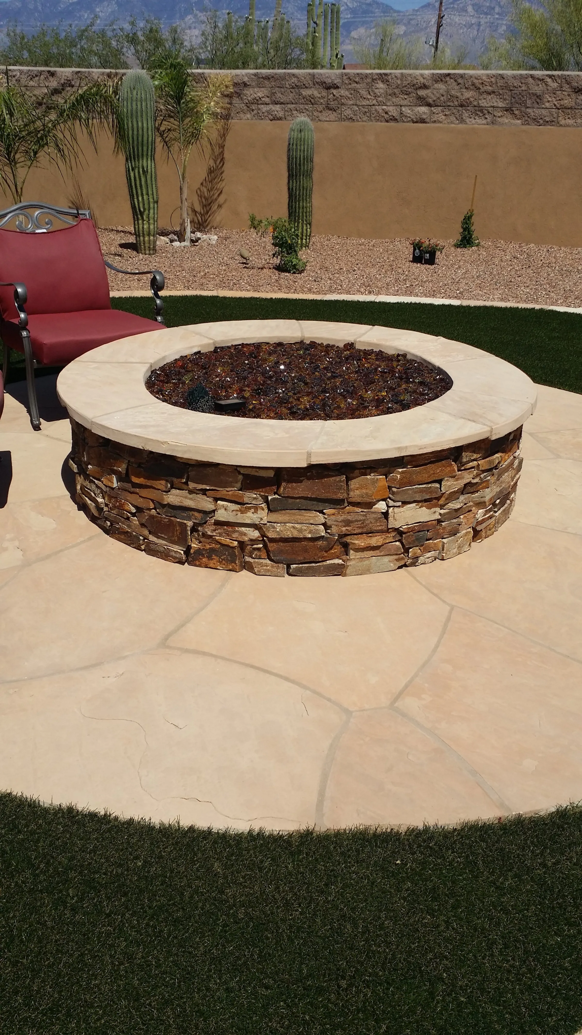 Stacked stone fire pit on a flagstone patio surrounded by turf and saguaros.