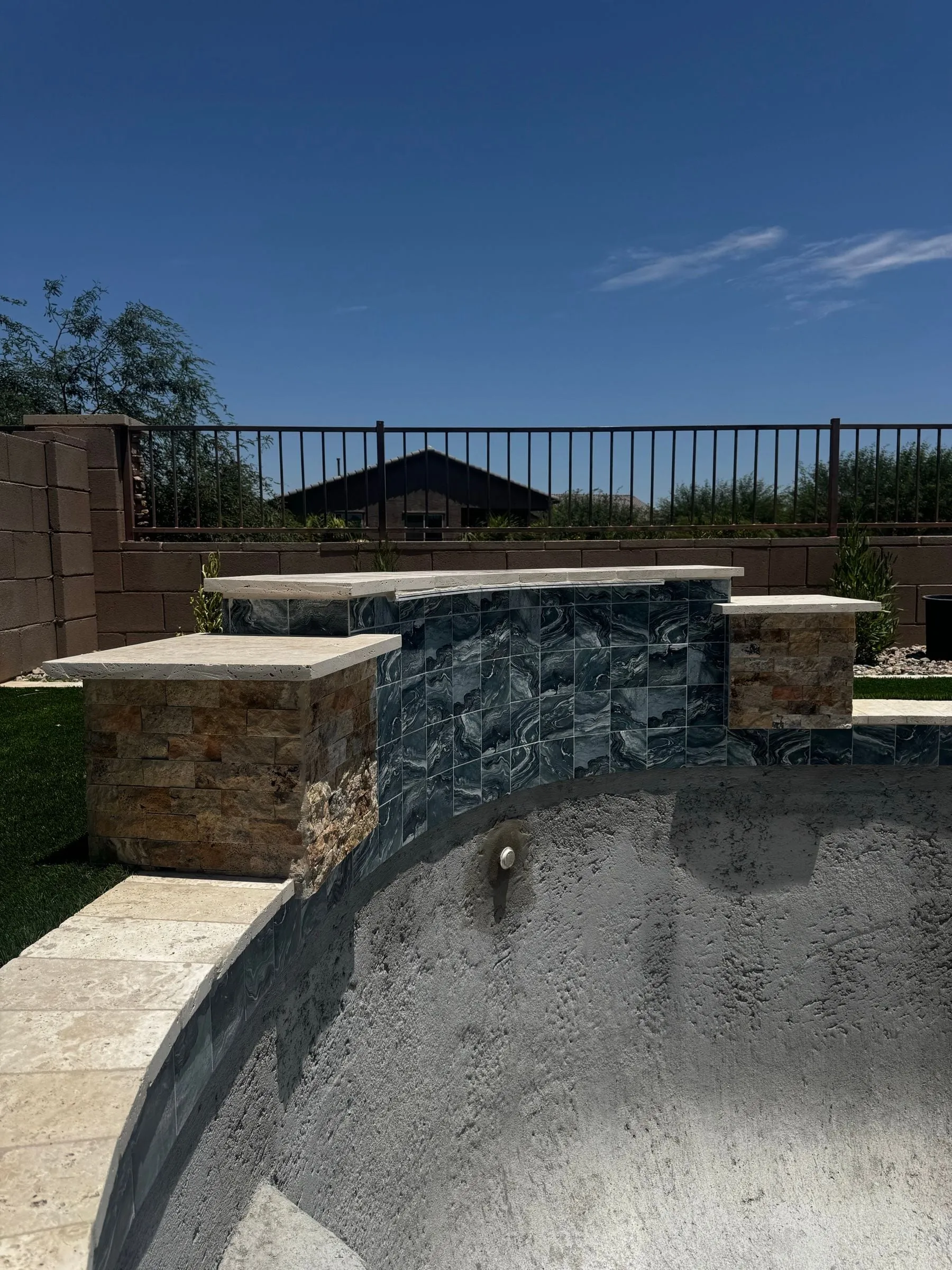 Raised pool wall with stacked stone pillars and dark mosaic tile above a freeform shell.