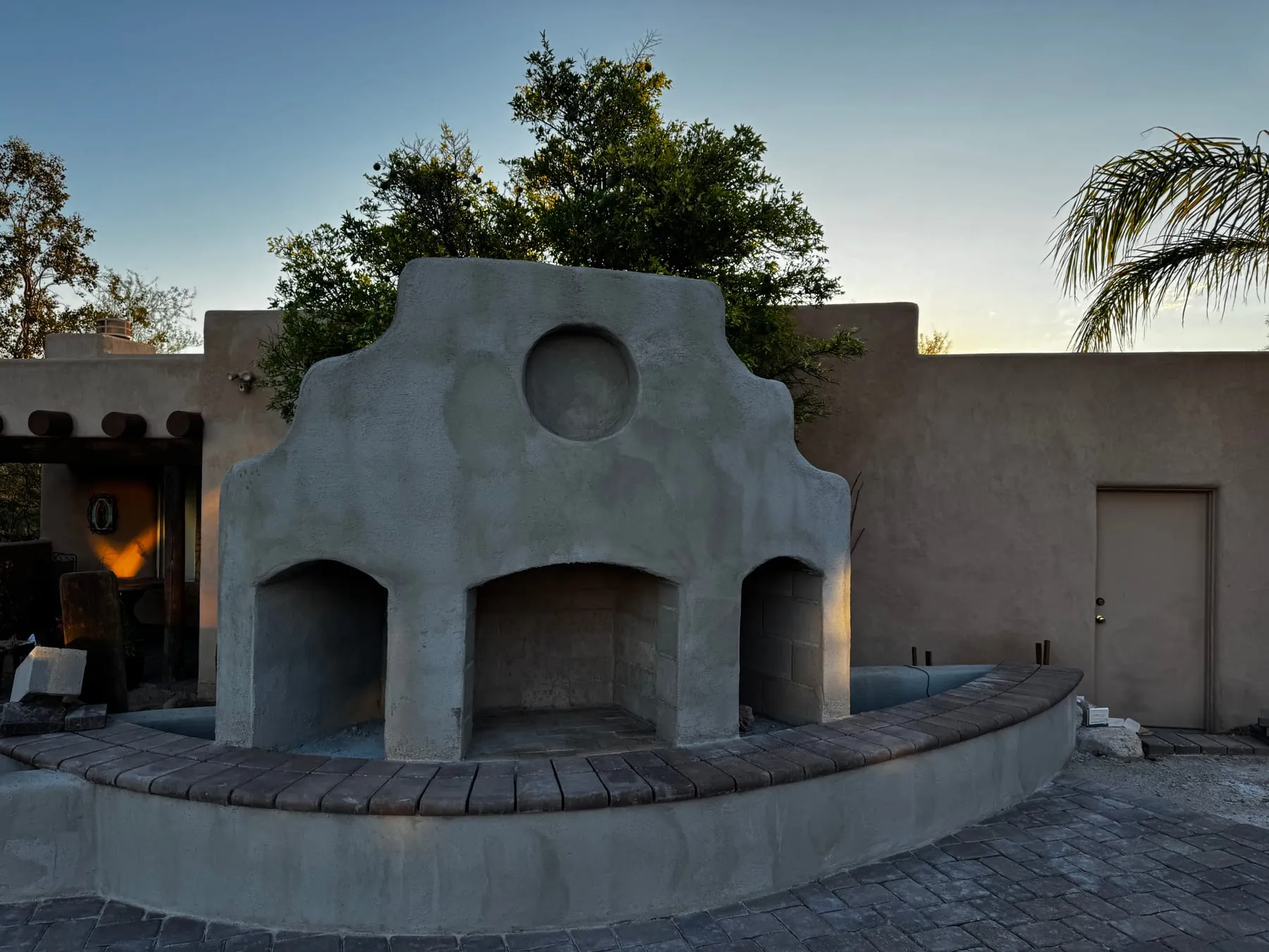 Stucco outdoor fireplace with arched openings and a capped curved seat wall.