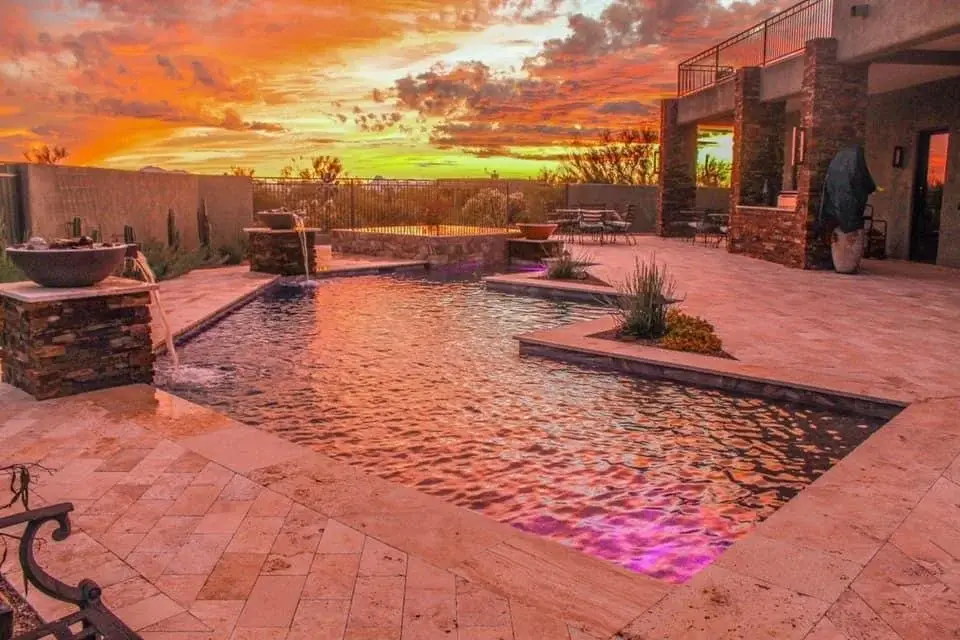Geometric pool at sunset with fire-and-water bowls on stacked stone pillars and travertine deck in Tucson.