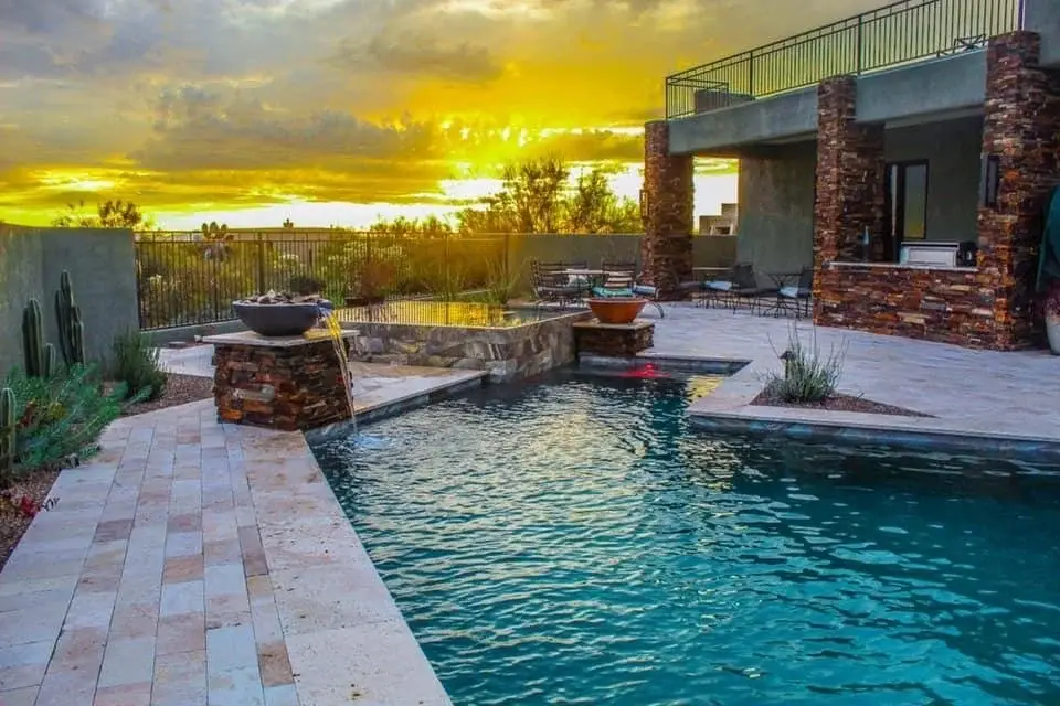 Pool and raised spa at sunset with fire-and-water bowls, stone columns and travertine walkways