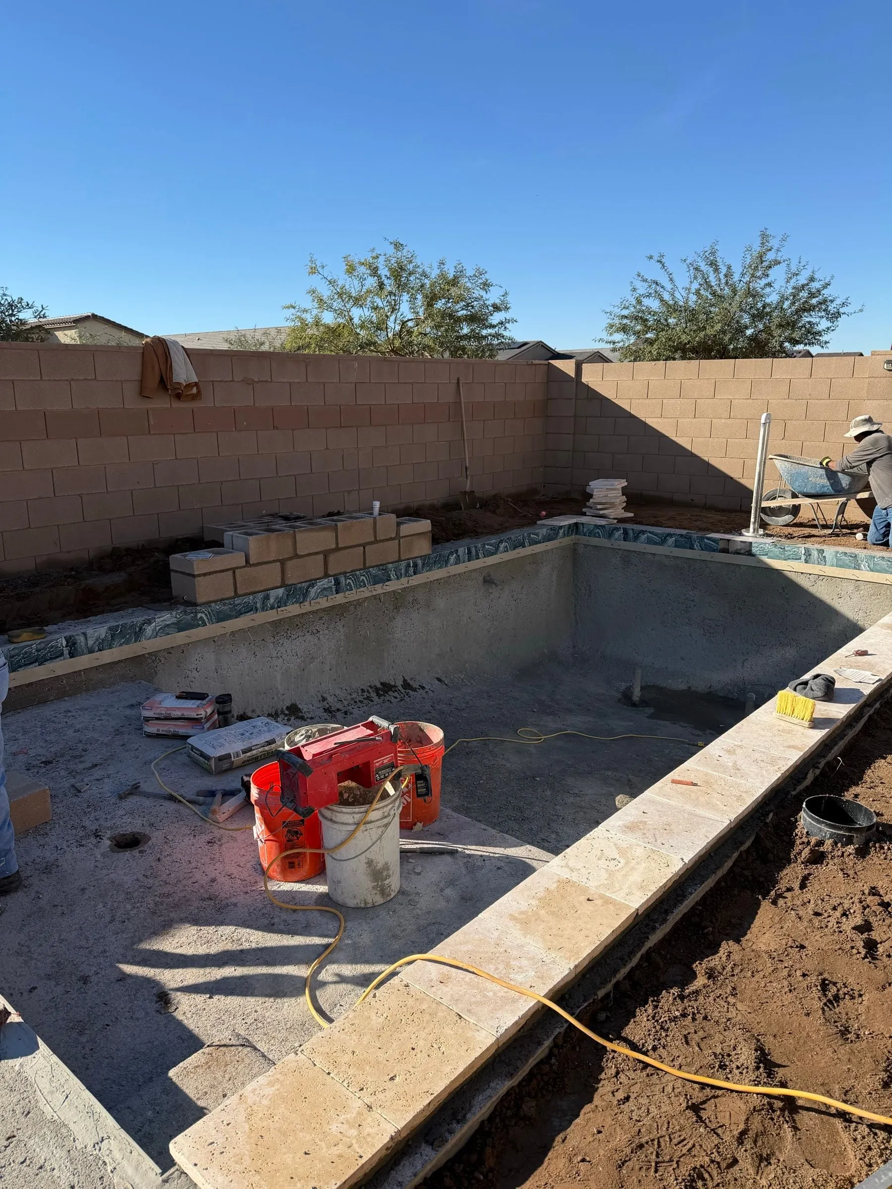 Travertine coping being installed around a rectangular pool shell with tile in place.