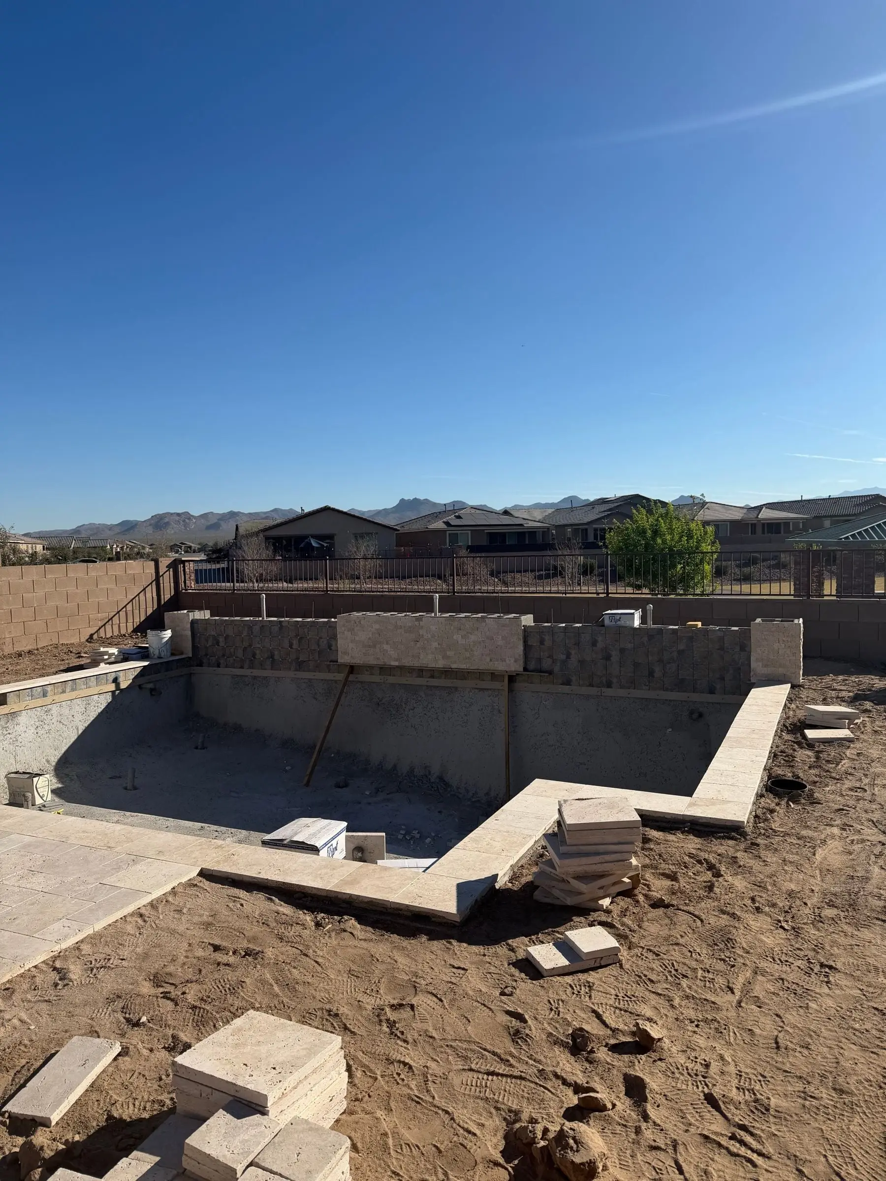 Travertine coping and a block raised wall going in around a new pool shell, Marana, AZ.