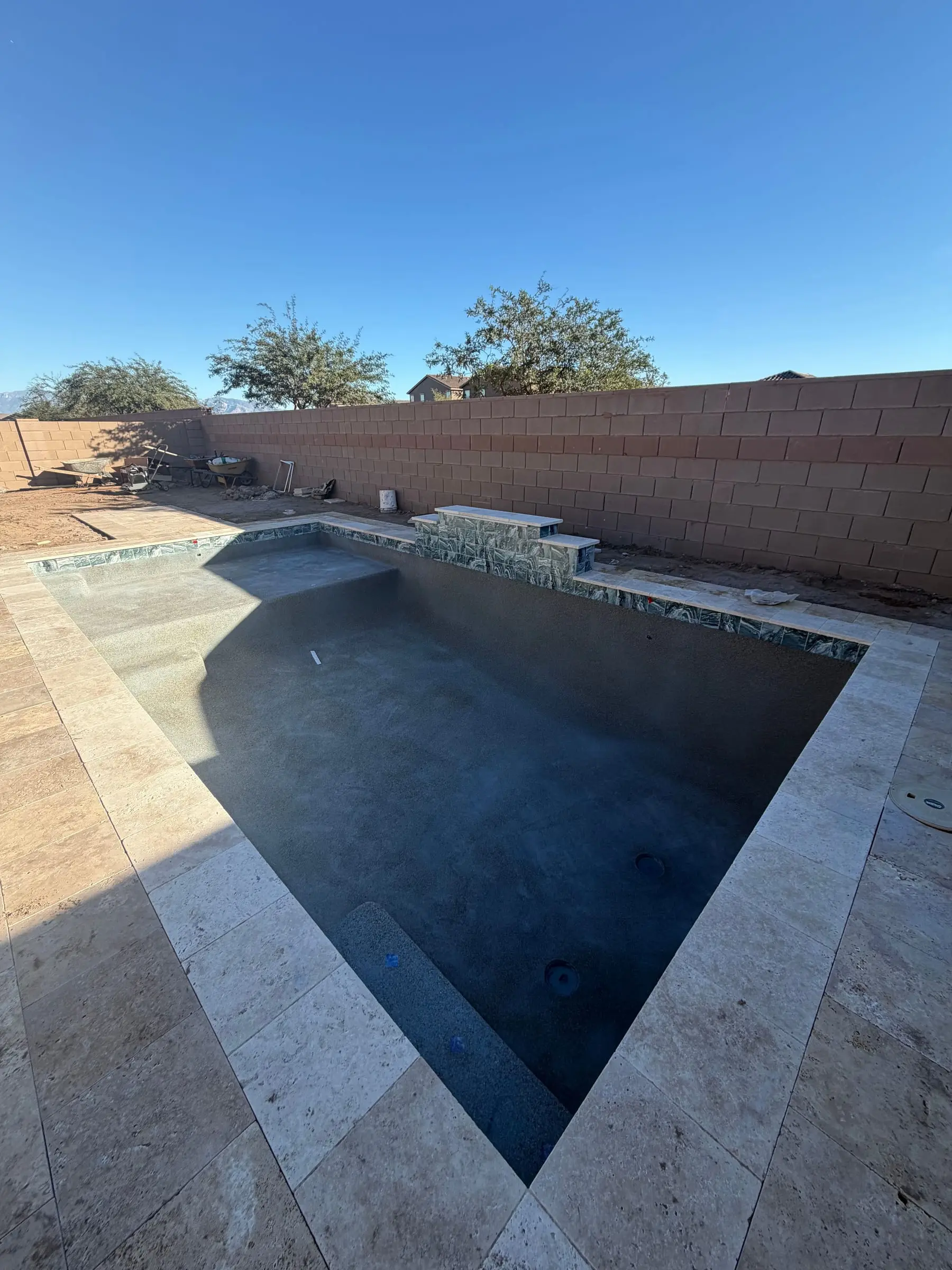 Travertine deck and coping finished around an empty pool shell with a mosaic tile line, Marana, AZ.