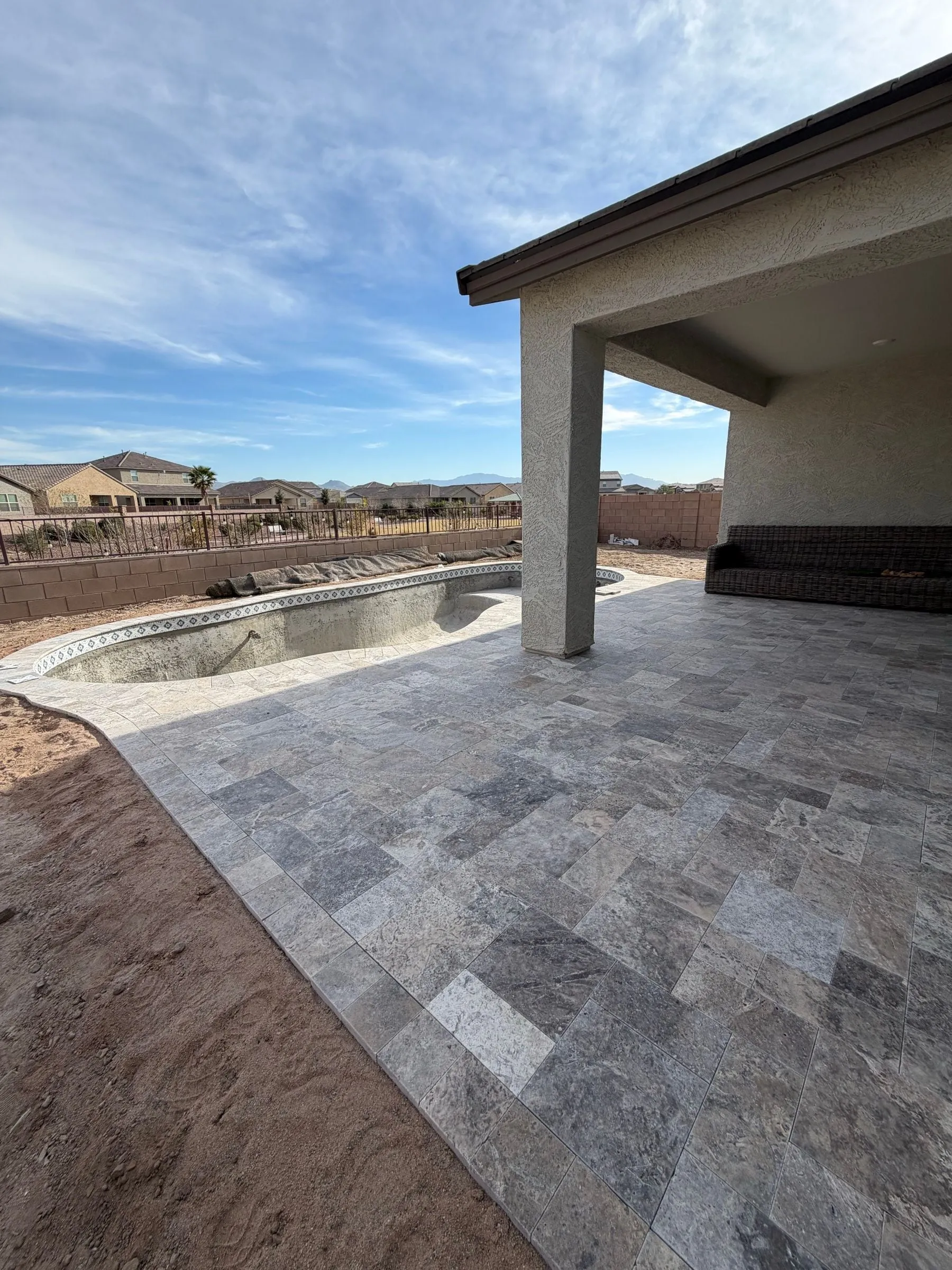 Travertine deck laid around a freeform pool shell next to a covered patio.