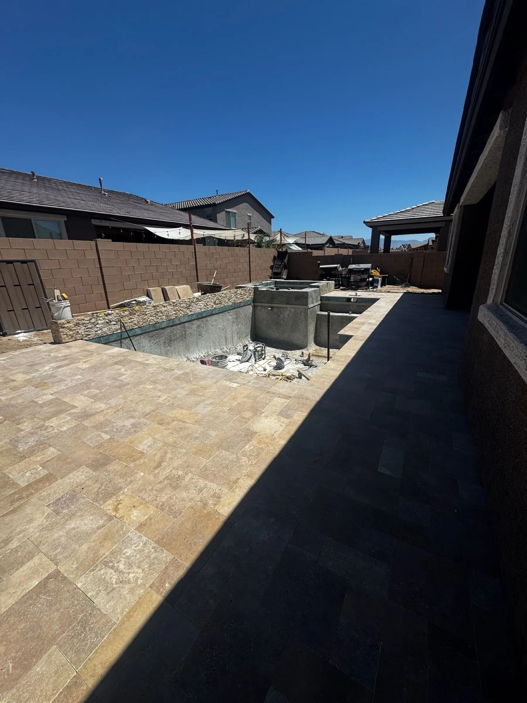 Travertine pavers laid along a rectangular pool shell beside a covered patio.