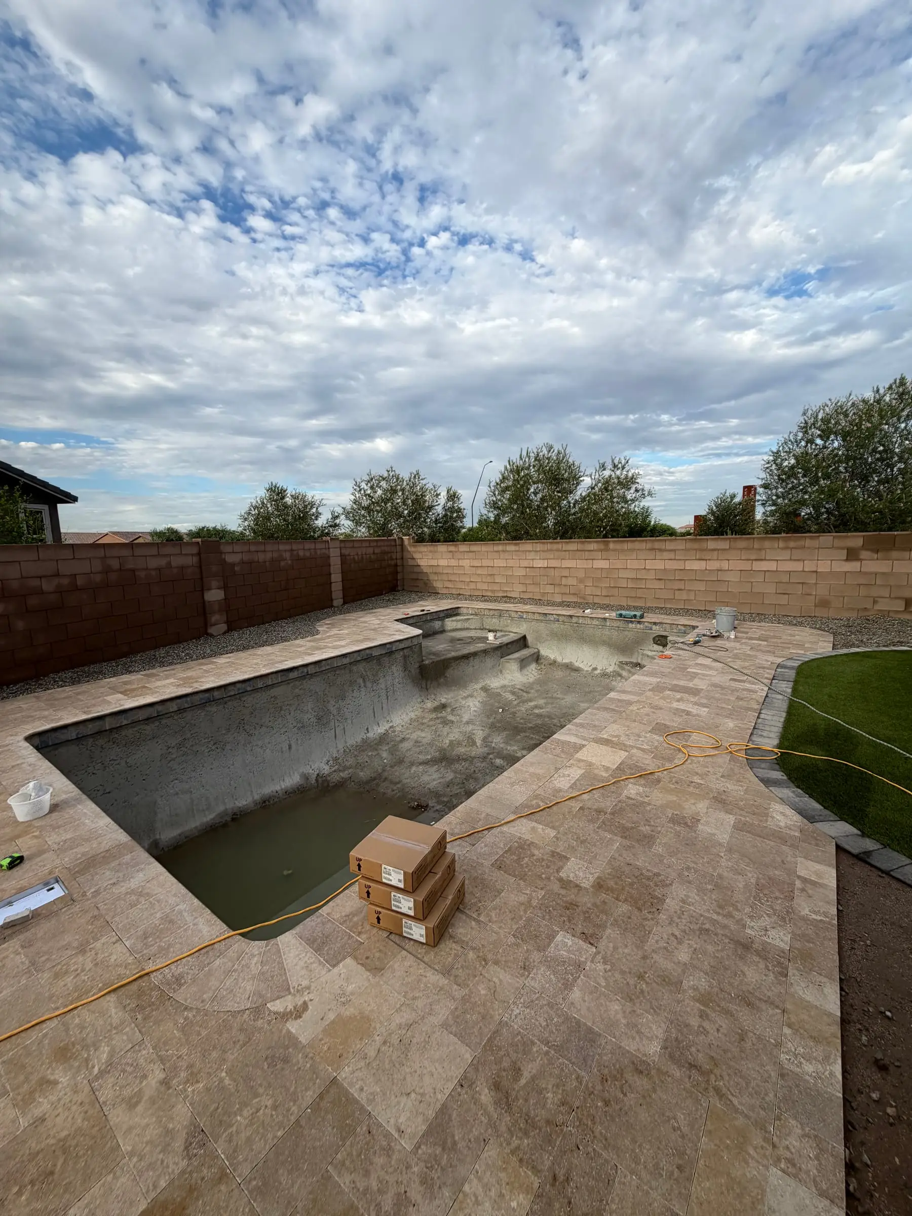 Travertine deck finished around a pool shell with entry steps.