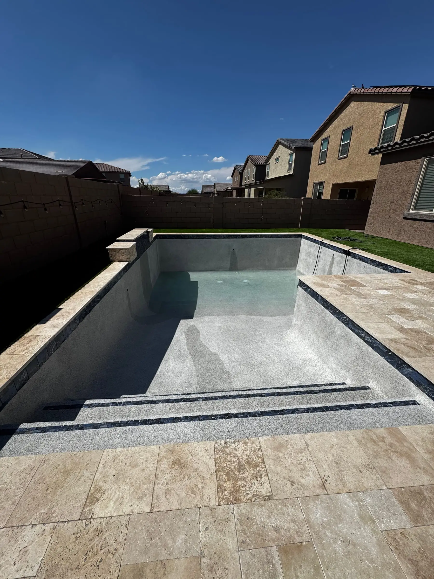 New travertine deck around a pool with wide entry steps, before the interior finish.