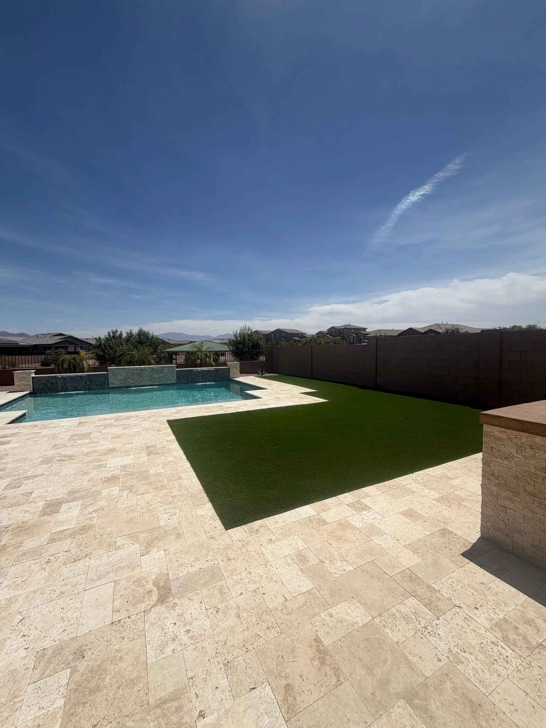 Finished Marana backyard with an ivory travertine deck, artificial turf and a pool with sheer descents.