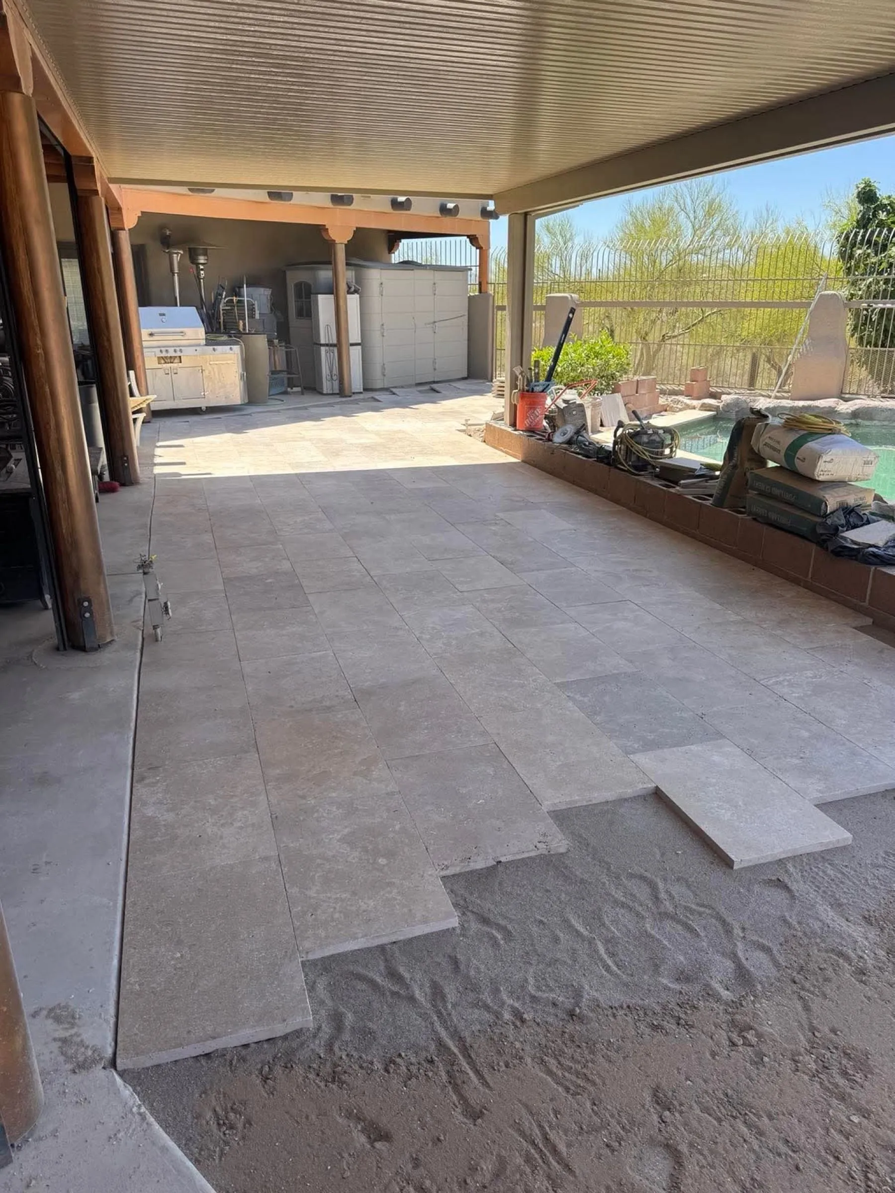 Travertine pavers being installed on a covered patio overlooking a pool.