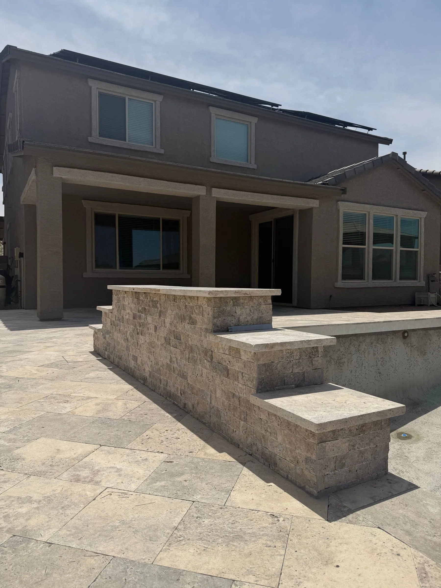Stepped raised wall clad in travertine beside a pool, with a matching travertine deck.