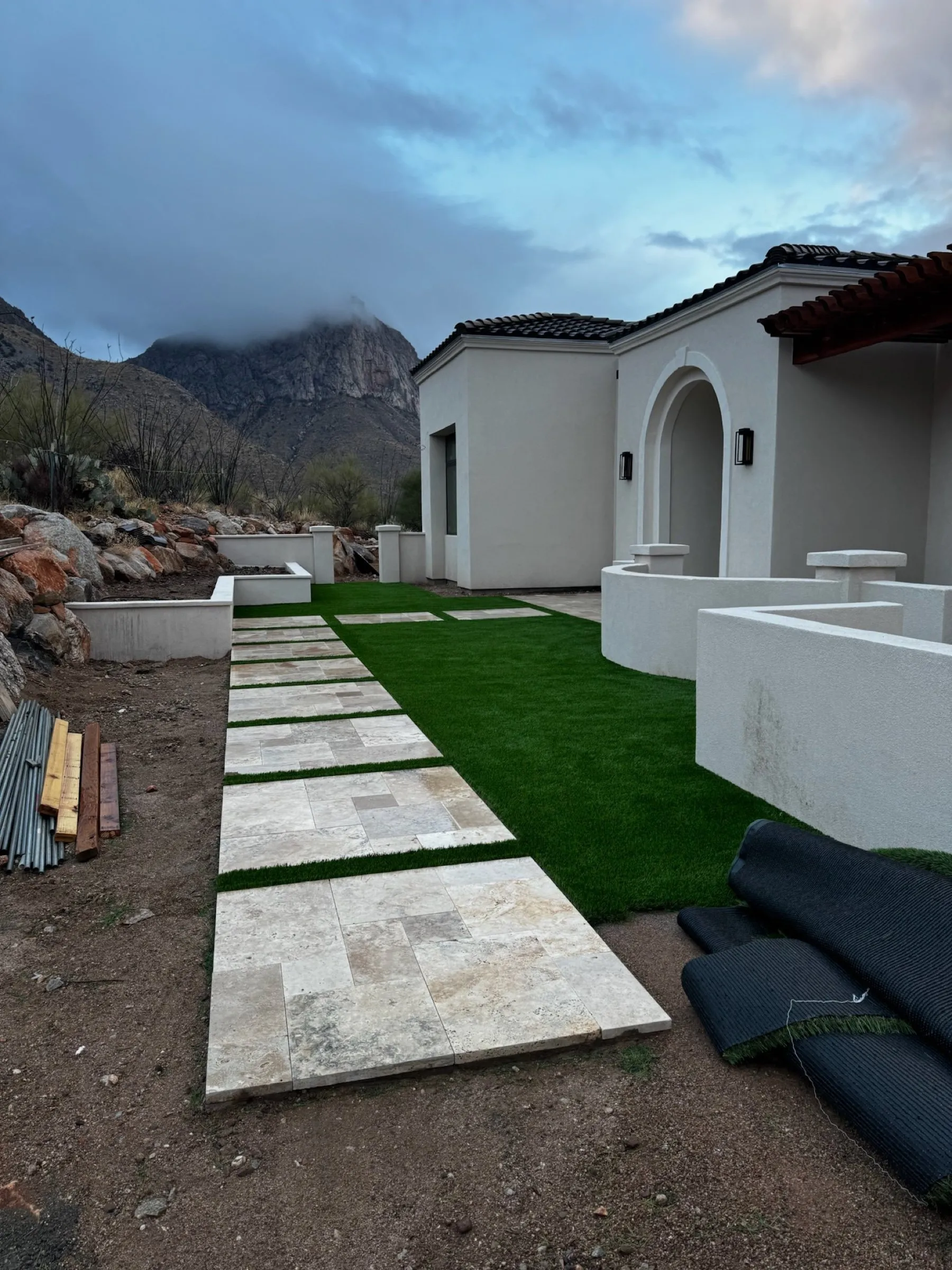 Travertine stepping pads and new turf being installed beside a home with mountain views in Oro Valley.