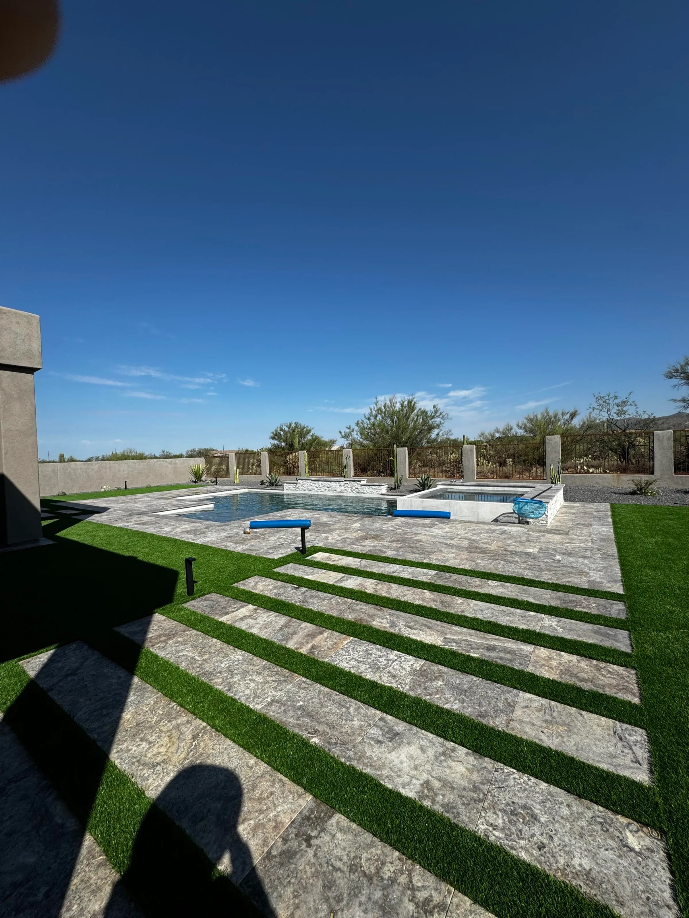 Travertine pavers with turf strips leading to a pool and raised spa.