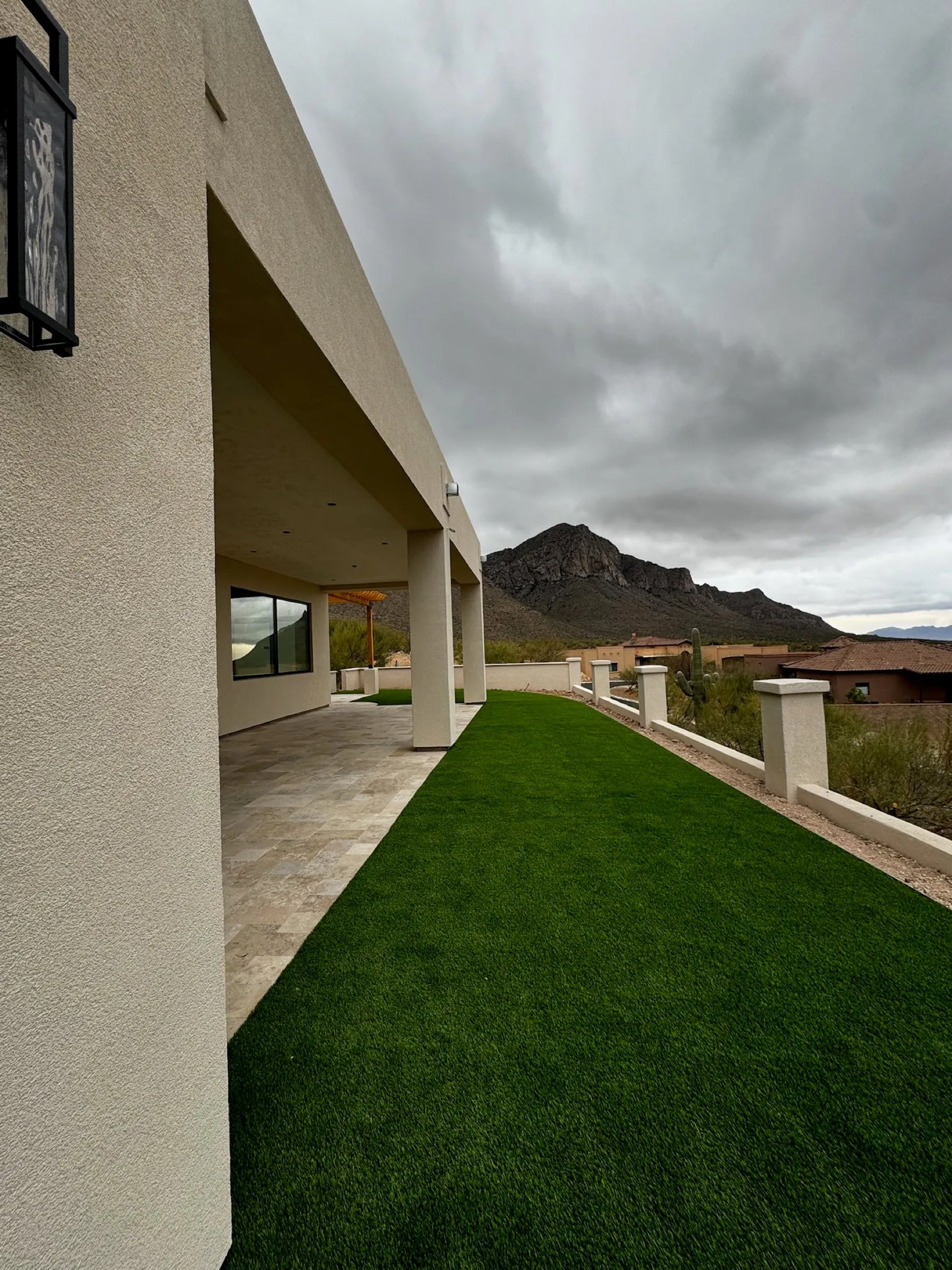 Artificial turf strip running along a travertine covered patio toward desert mountains
