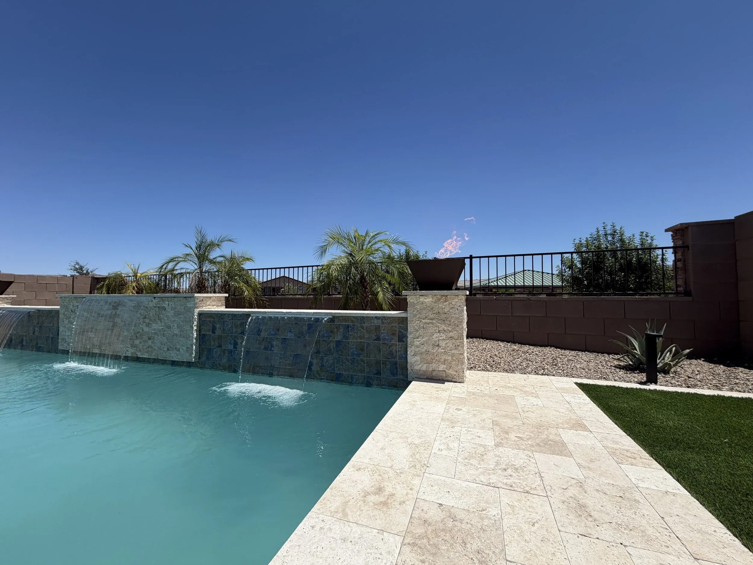 Wide view of twin sheer descents, a fire bowl pillar, travertine deck and artificial turf.