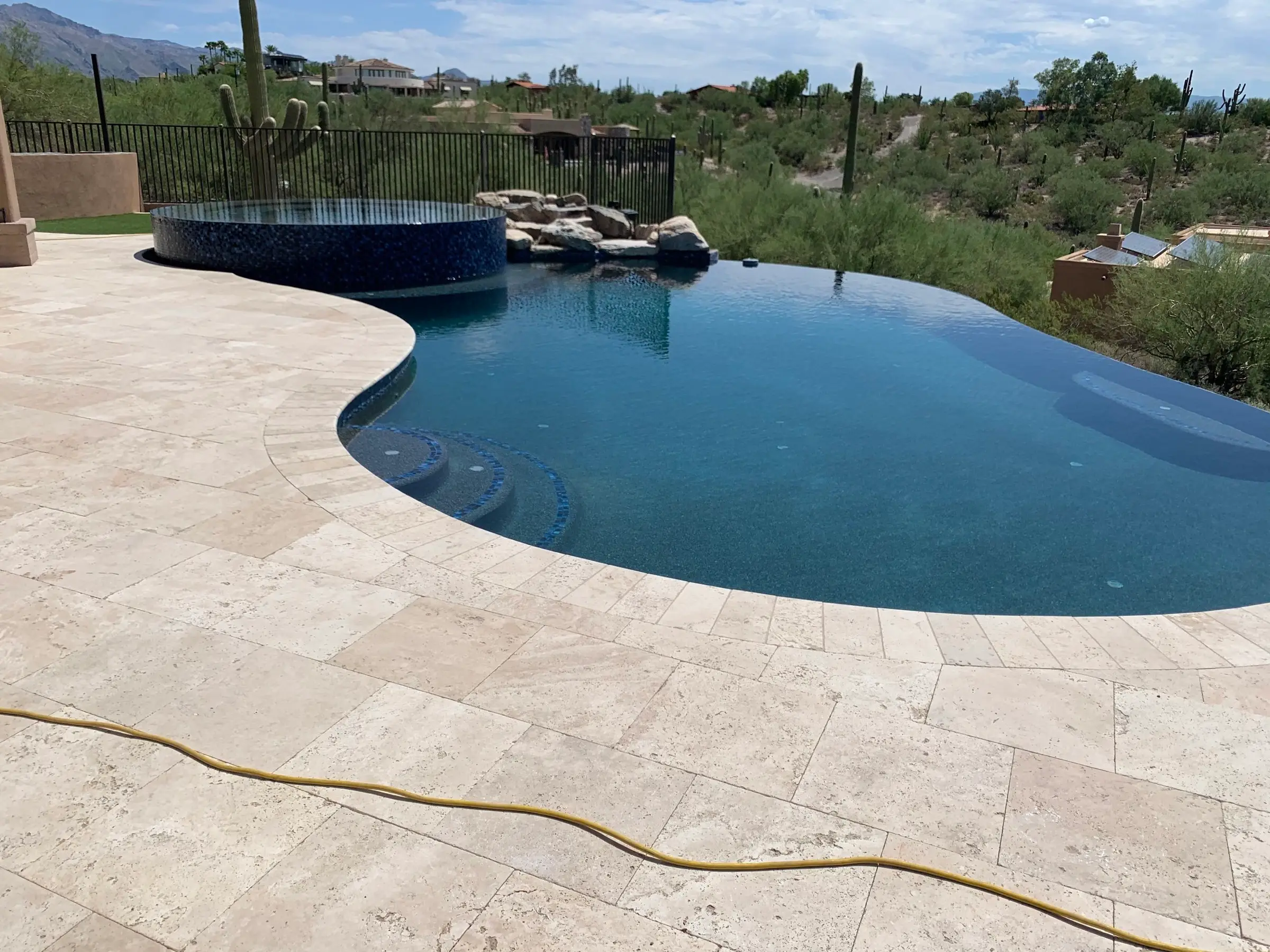 Freeform vanishing edge pool with raised round spa, boulder waterfall and travertine deck overlooking the Tucson desert.