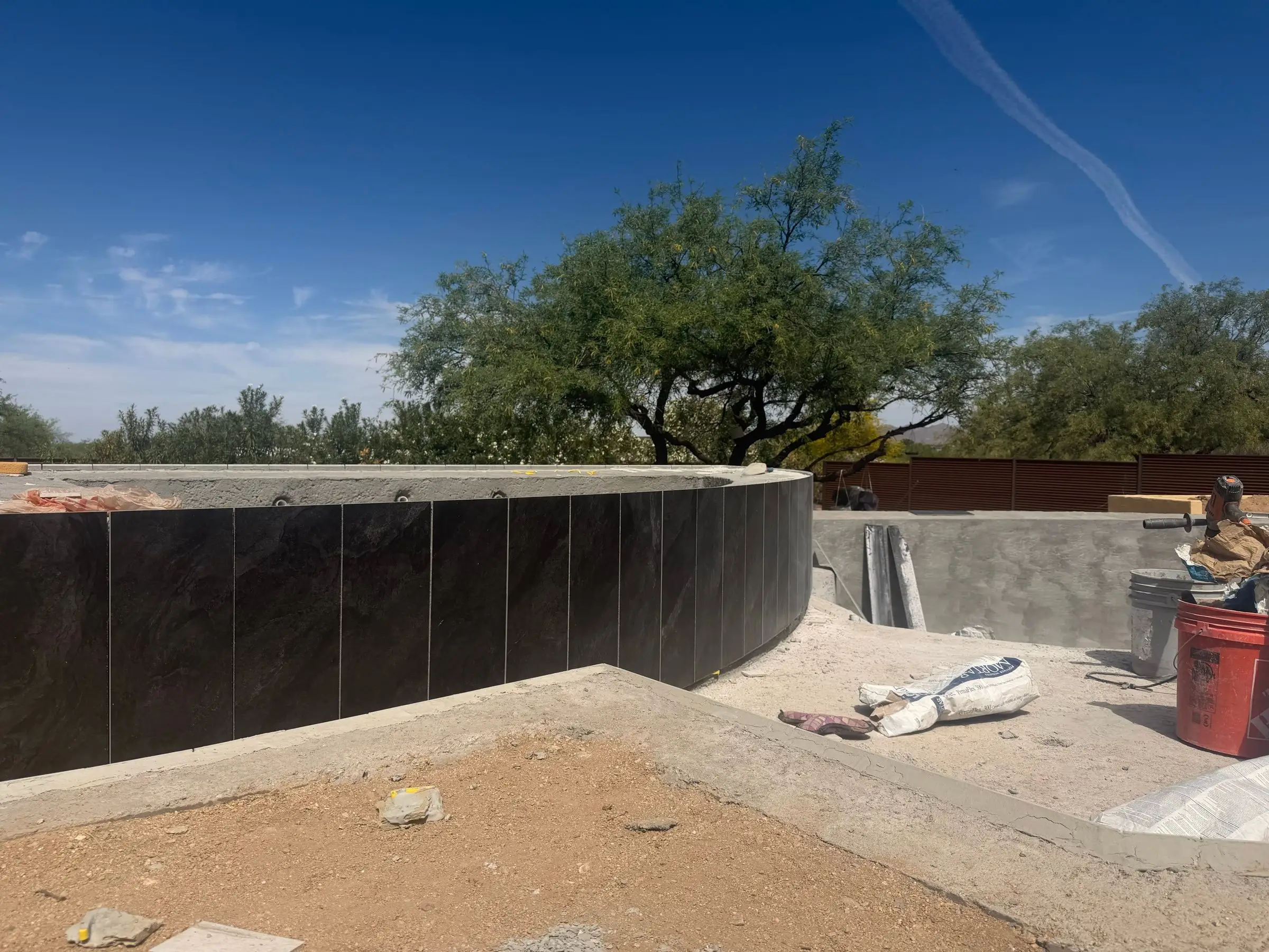 Dark tile installed on the curved vanishing-edge wall of a pool under construction