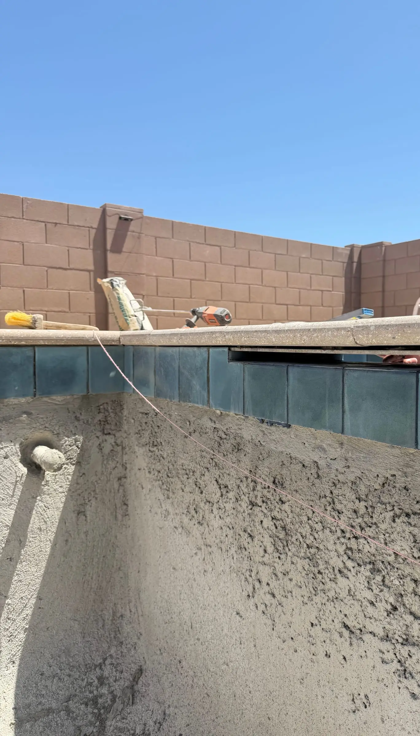 Dark waterline tile being set below the coping on a new shotcrete pool shell, Gladden Farms in Marana, AZ.