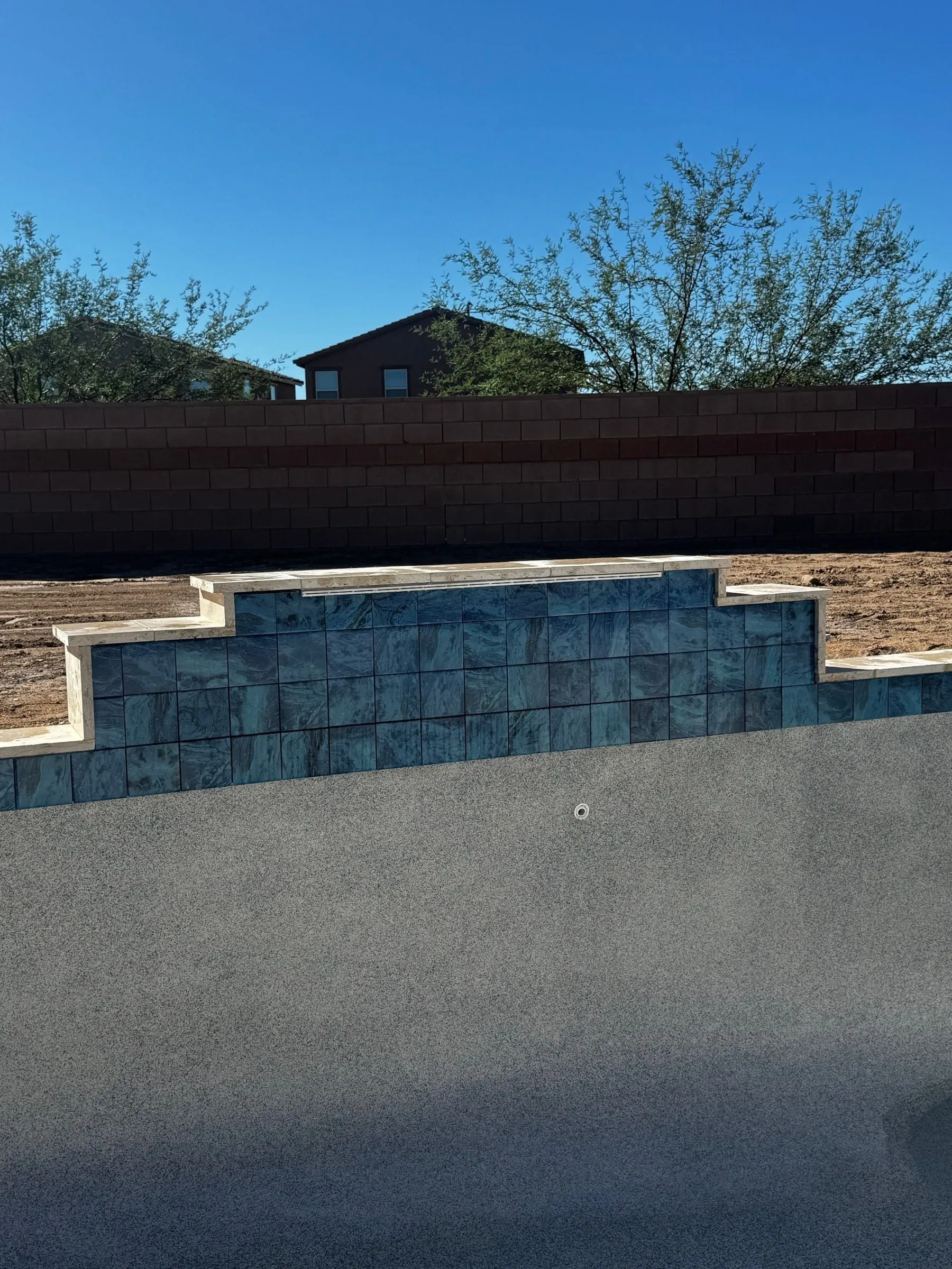 Blue waterline tile follows a stepped raised wall above freshly finished pool surfaces.